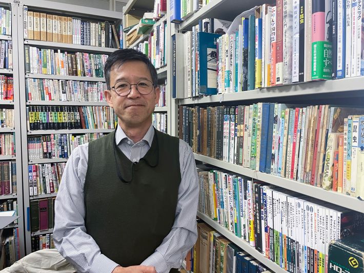 図鑑に囲まれる斎木 健一さんの写真