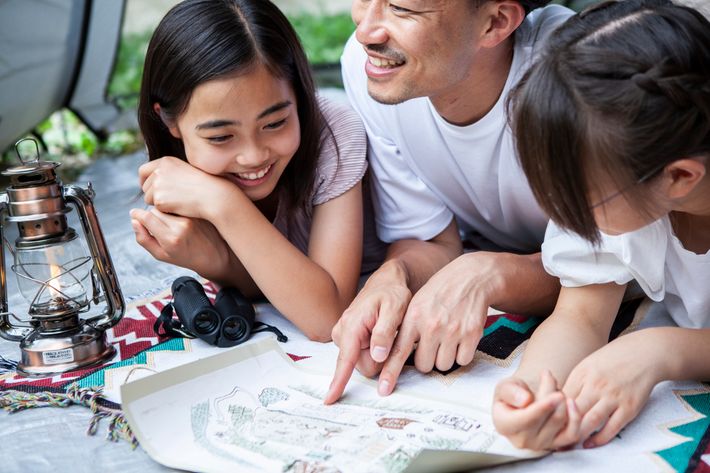 父親と二人の娘が地図を指さしながらアウトドアの計画を立てる様子