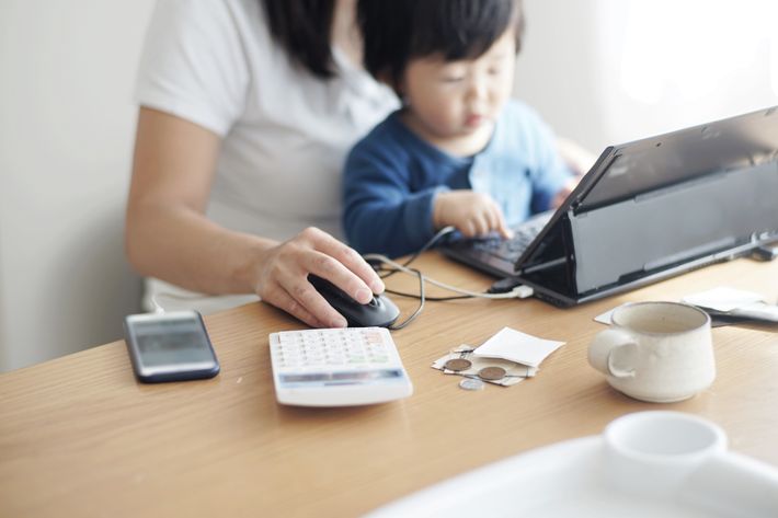 女性が子どもを膝に乗せながらタブレットと電卓で作業している