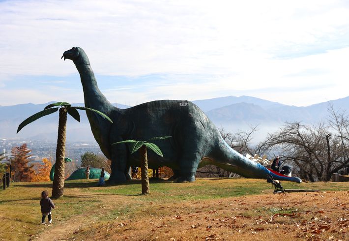 大パノラマの中に鎮座する大きな恐竜を見上げる小さな子どもの写真。